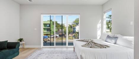 A bedroom with a bed, a window, a door, and a view of the outside.