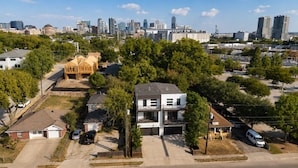 A residential area with a two-story house, a construction site, and a city skyline in the background. - Dallas LUXE 4BR, 4 Kings, Hot Tub, Outdoor Theater (Dallas)