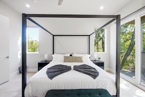 Een moderne slaapkamer met een hemelbed, een nachtkastje met een lamp, en uitzicht op groen door grote ramen.