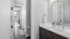A modern bathroom with a large mirror, white sink, and dark wooden cabinets. - Dallas LUXE 4BR, 4 Kings, Hot Tub, Outdoor Theater (Dallas)