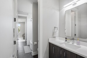 Een moderne badkamer met een grote spiegel, een witte wastafel en donkere houten kastjes.