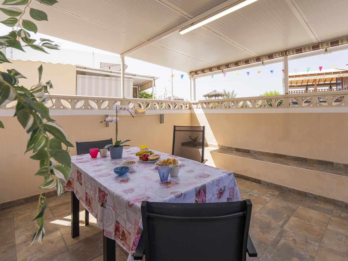 Een terras buiten met een eettafel, omgeven door potplanten en een decoratieve schutting.
