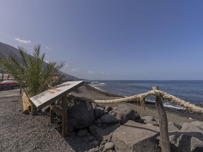 Ein felsiger Strand mit einem Holzschild, Palmen und einer Seilsperre.
