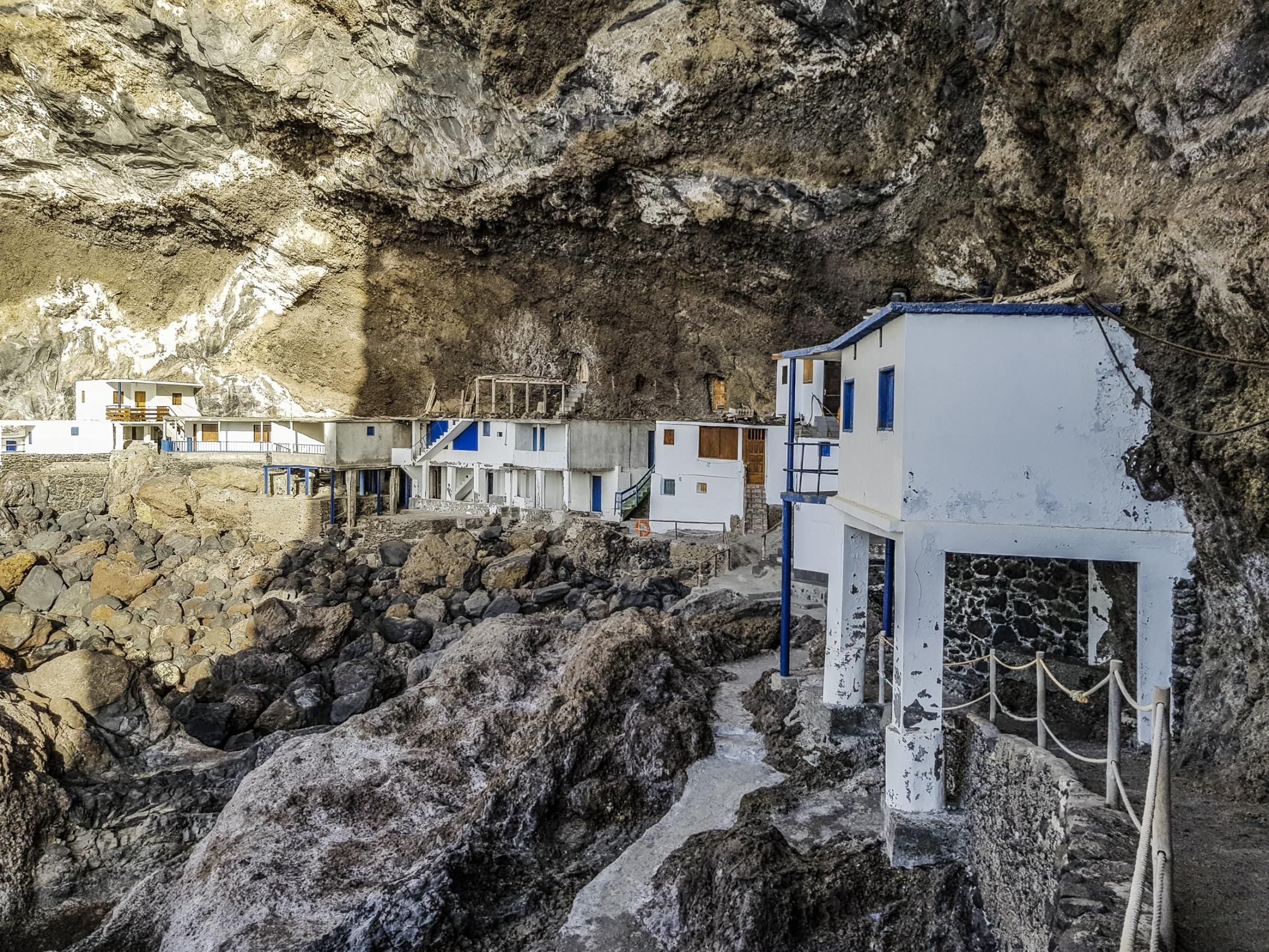 Un hôtel en bord de mer, avec des bâtiments blancs et des touches de bleu, situé sur un terrain rocheux, avec une sorte de grotte en arrière-plan.