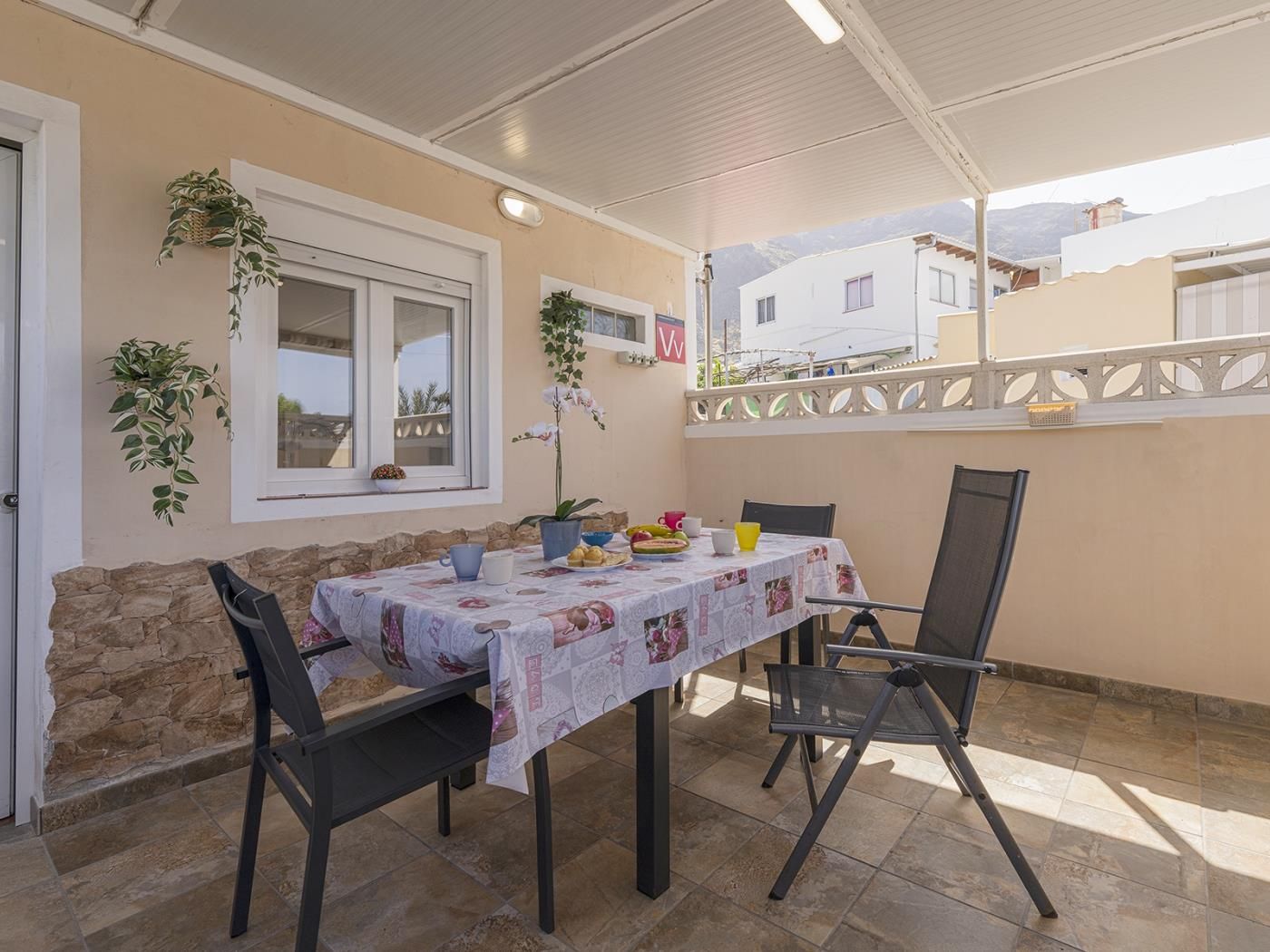 Une terrasse extérieure avec une table dressée pour deux personnes, entourée de murs en pierre et d’une clôture blanche.