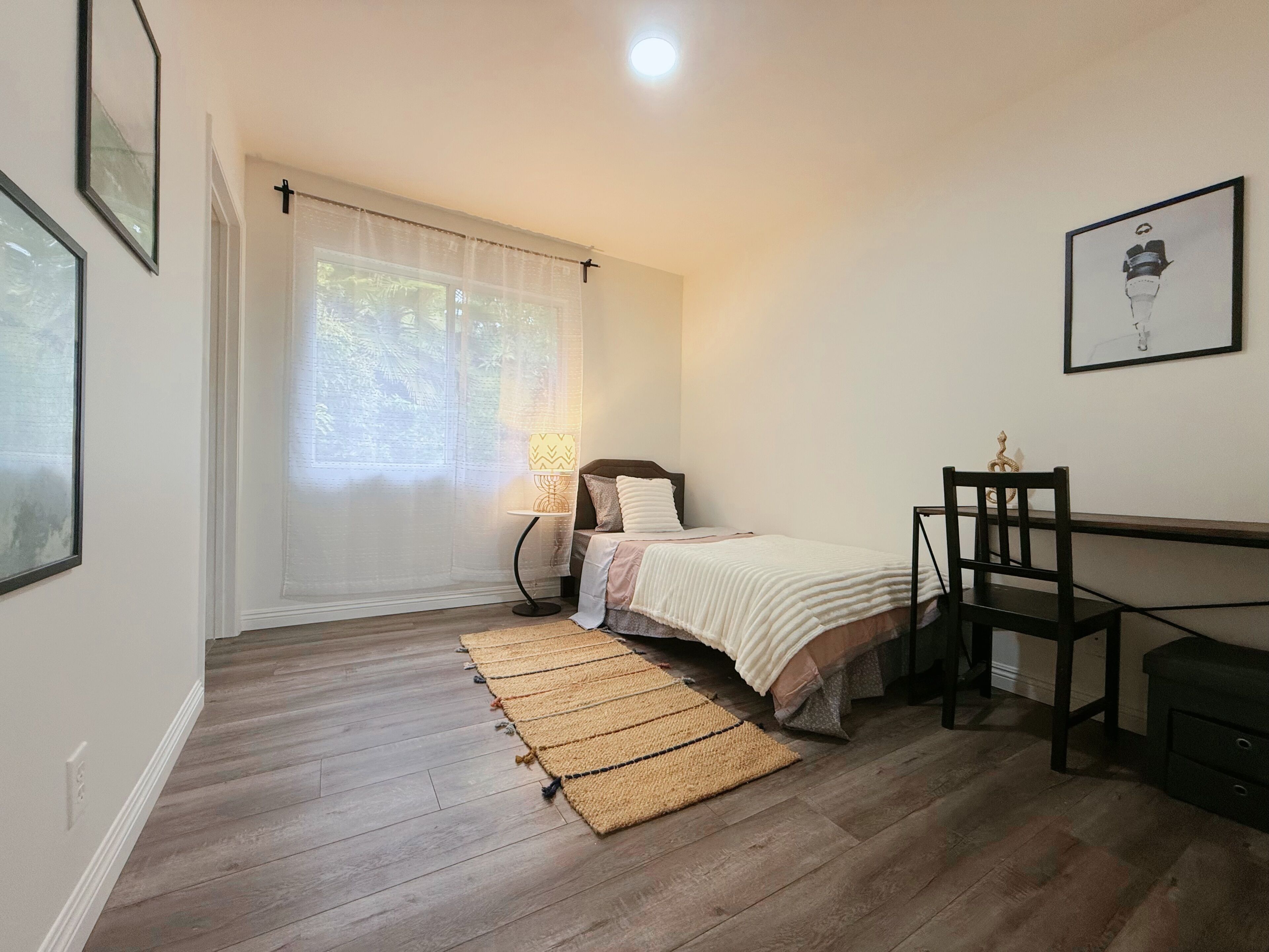 A bedroom with a bed, a desk, a chair, a lamp, and a window with curtains.
