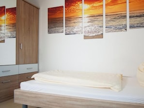 Une chambre à coucher avec un lit en bois, une armoire et trois tableaux représentant des couchers de soleil accrochés au mur.