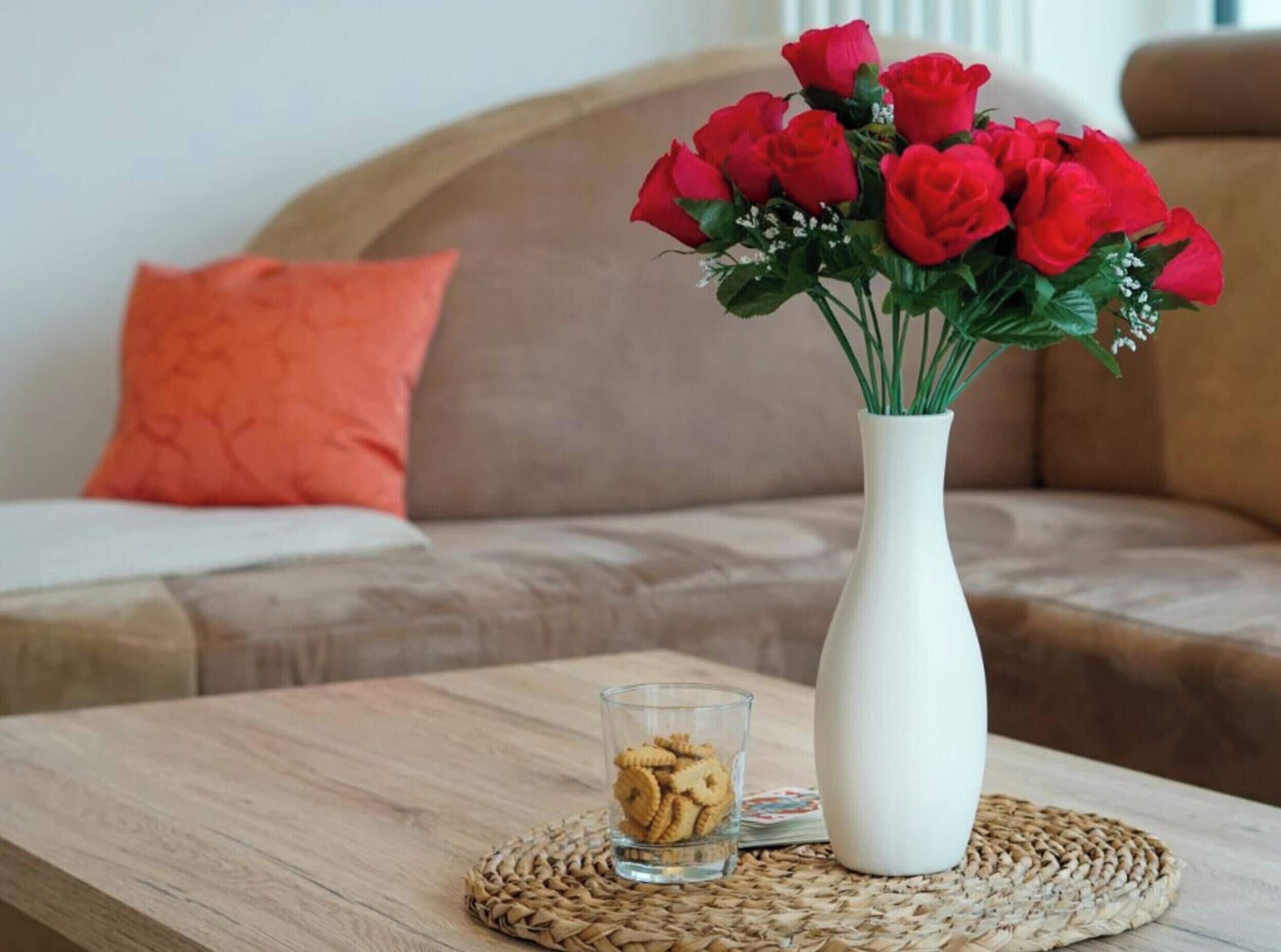 A white vase with red roses on a wooden table.