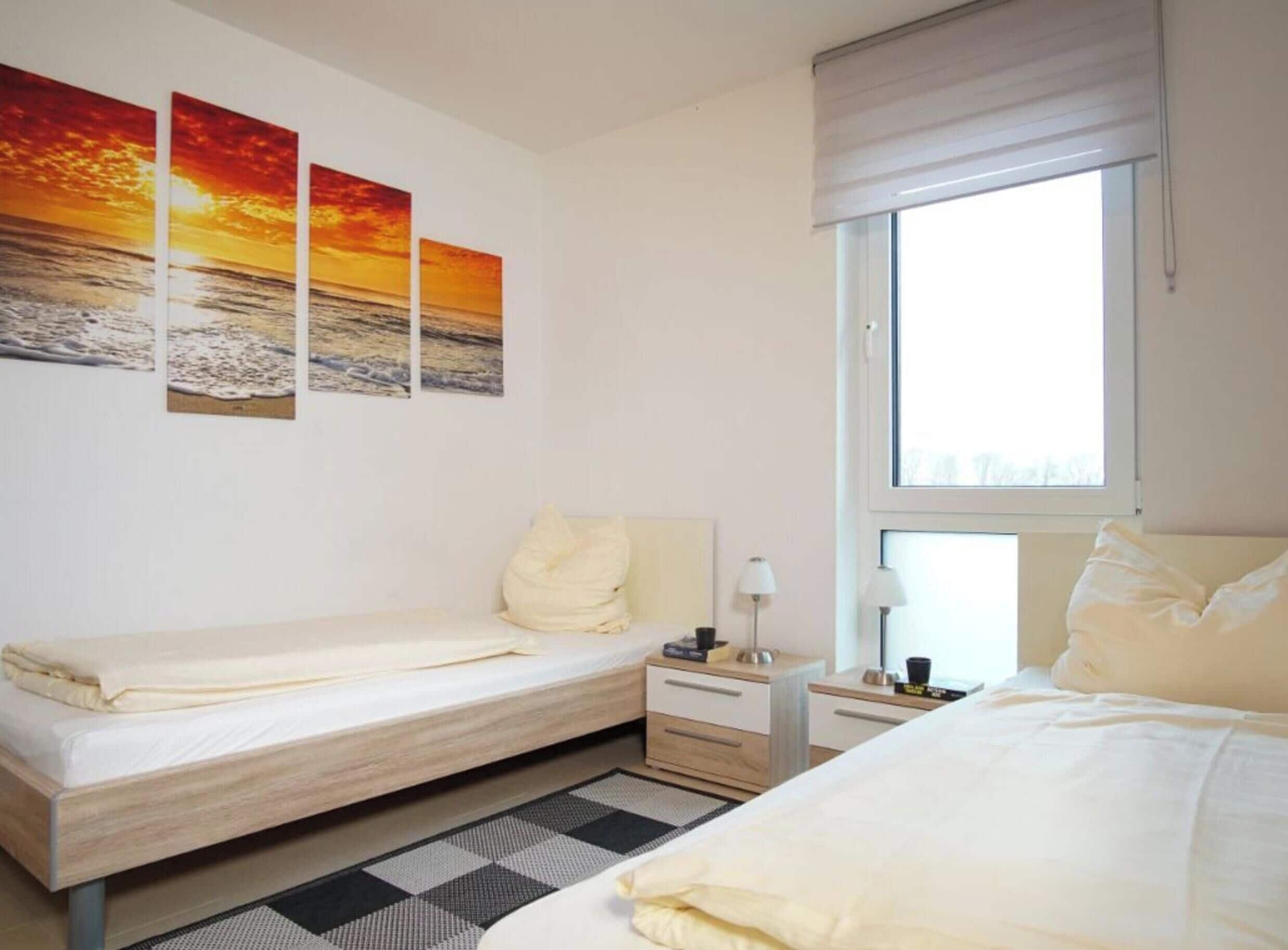 Een hotelkamer met twee bedden, een geruit tapijt, een raam met zonwering en drie zonsondergangschilderijen aan de muur.
