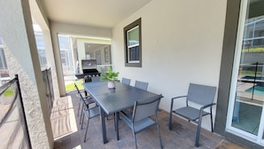 Eine Außenpatio mit Tisch und Stühlen, einem Grill und Blick auf einen Swimmingpool.