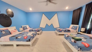 Ein Hotelzimmer mit zwei Betten, einer großen, M-förmigen Wanddekoration und Bettwäsche mit Mickey Mouse-Motiven.