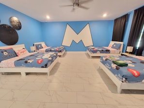 A hotel room with two beds, a large M-shaped wall decoration, and Mickey Mouse-themed bedding. - Spacious 8-bedroom house in amazing Four Corners with AC (Four Corners)