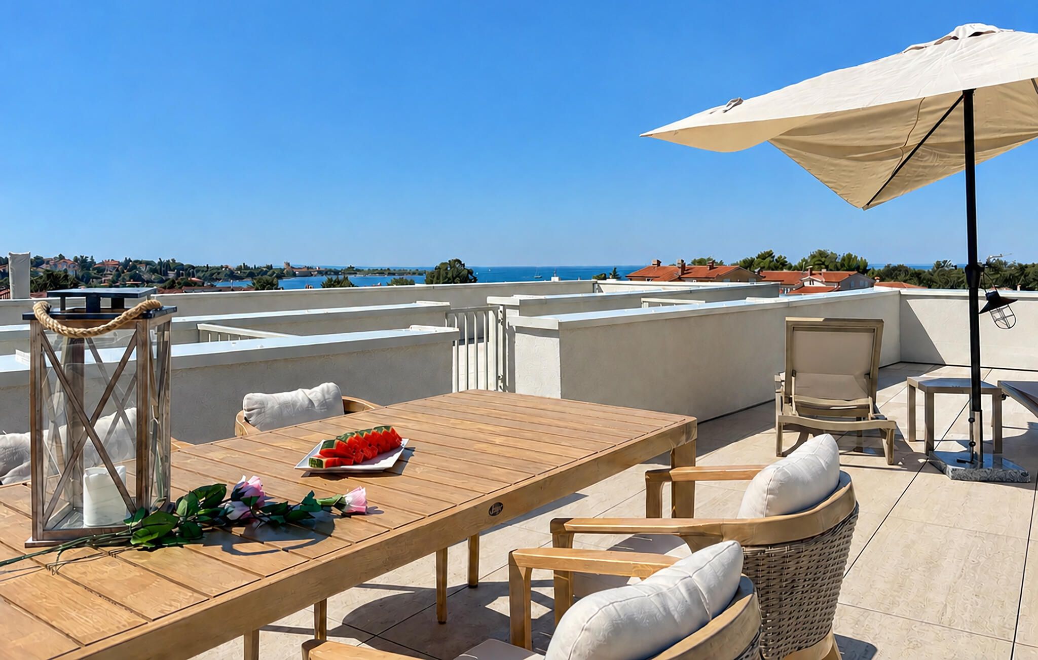 Une terrasse sur le toit avec une table en bois, des chaises, une lanterne et une vue sur la mer.