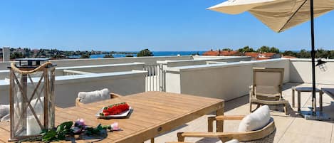 A rooftop terrace with a wooden table, chairs, a lantern, and a view of the sea.
