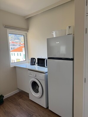 A compact kitchen with a washing machine, a microwave, and a refrigerator. - Maria Beach (Machico)