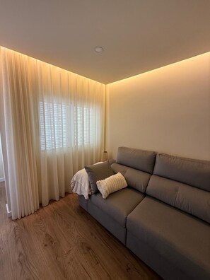 Ein modernes Wohnzimmer mit einem grauen Sofa, einer weißen Decke und transparenten Vorhängen.