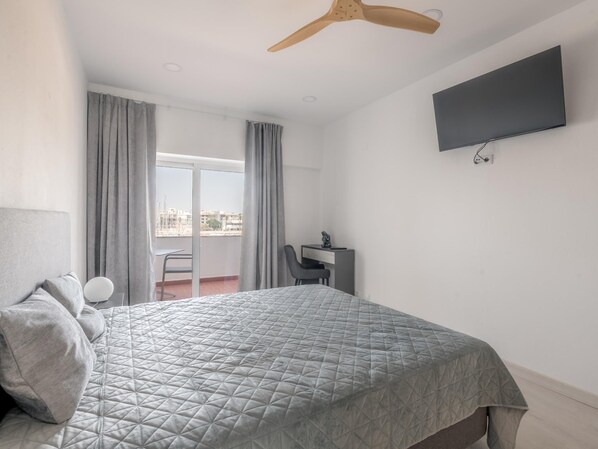 Ein Hotelzimmer mit Bett, Schreibtisch, Stuhl, Fernseher und einem Balkon mit Vorhängen.