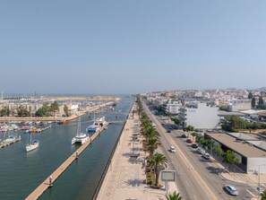 Ein Yachthafen mit vertäuten Booten, eine Straße parallel zum Wasser und Gebäude im Hintergrund.