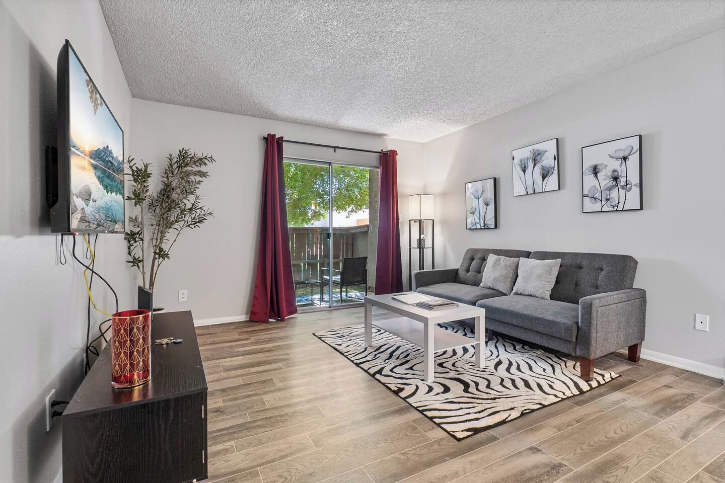 A modern living room with a grey sofa, a coffee table, a zebra-pattern rug, and a flat-screen TV mounted on the wall.