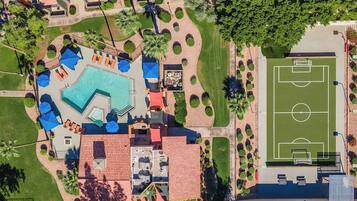 An aerial view of a resort with a swimming pool, lounge areas, and a soccer field.