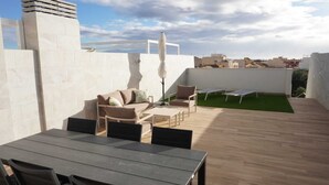 Eine Terrasse im Freien mit Tisch, Stühlen, einer Sitzecke und einem kleinen Rasenstück.