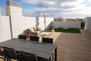 Un patio exterior con una mesa y sillas, un sofá y una pequeña zona de césped.