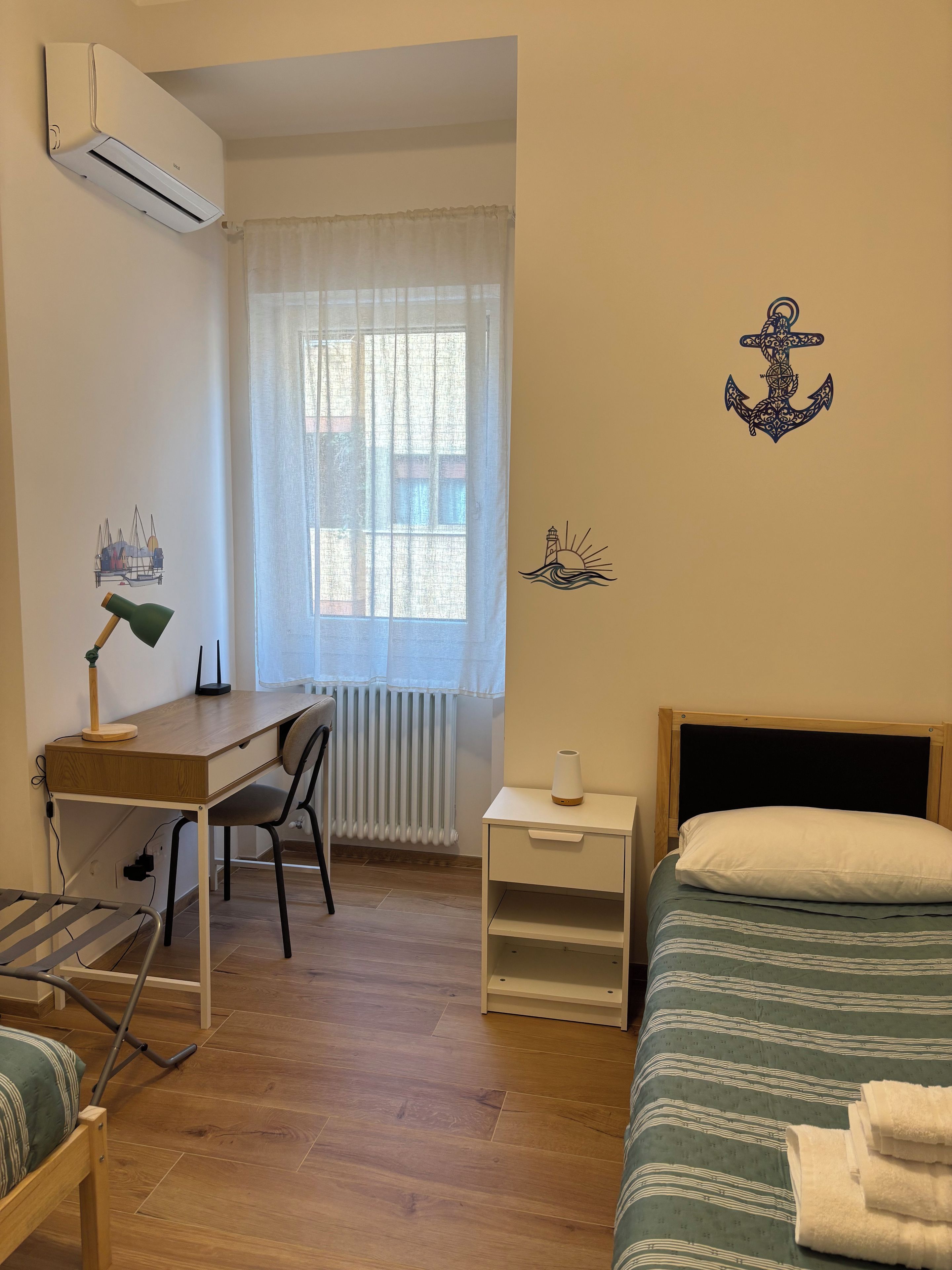 A bedroom with a bed, a desk, a chair, a radiator, and a window with curtains.