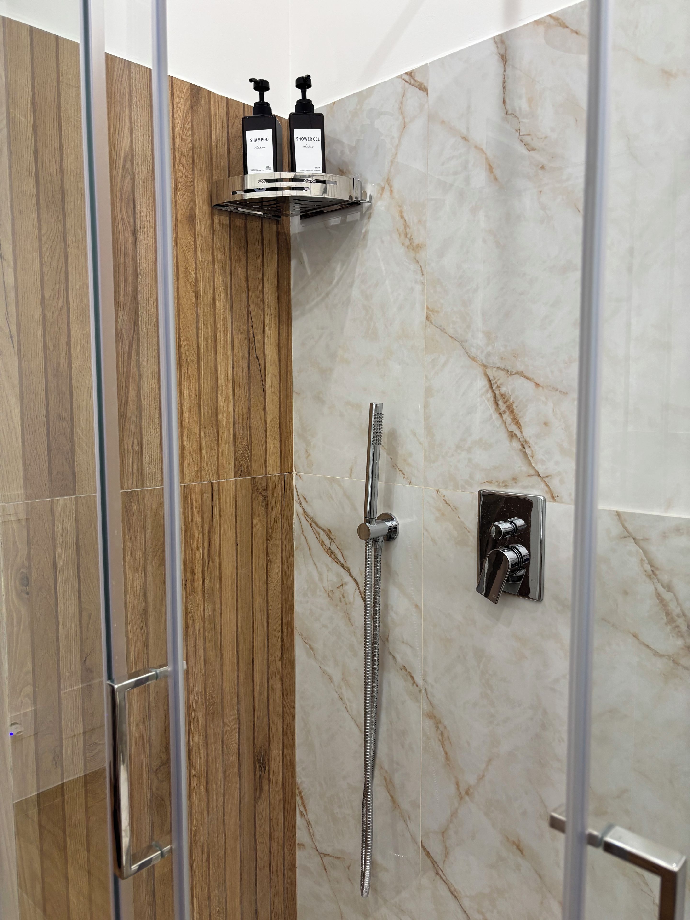 A shower with a handheld showerhead and a wall-mounted control panel.