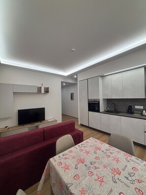 A modern living room with a flat-screen TV, a red sofa, and a dining table with a marine-themed tablecloth. - Comfort Miranda House Ostia: Getting to Rome and the Airport (Lido di Ostia)