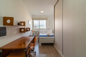 A compact hotel room with a wooden desk, a single bed, and a window with a view. - 2BR Apt Just 10 Mins From Barra da Tijuca Beach Vlm905 (Rio de Janeiro)