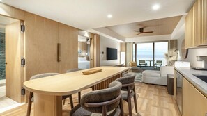 Ein modernes Hotelzimmer mit großem Esstisch, Sitzgelegenheiten, einer Küchenzeile, einem Fernseher und Blick aufs Meer.