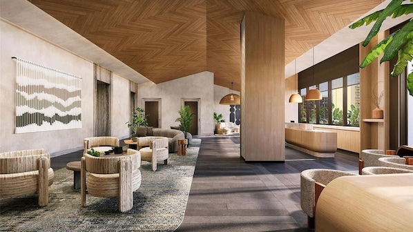 Un hall d’entrée spacieux avec un plafond haut, un plancher en bois et une colonne centrale. On y trouve des coins salon avec des chaises et des tables, ainsi qu’une grande fenêtre qui laisse entrer la lumière naturelle.