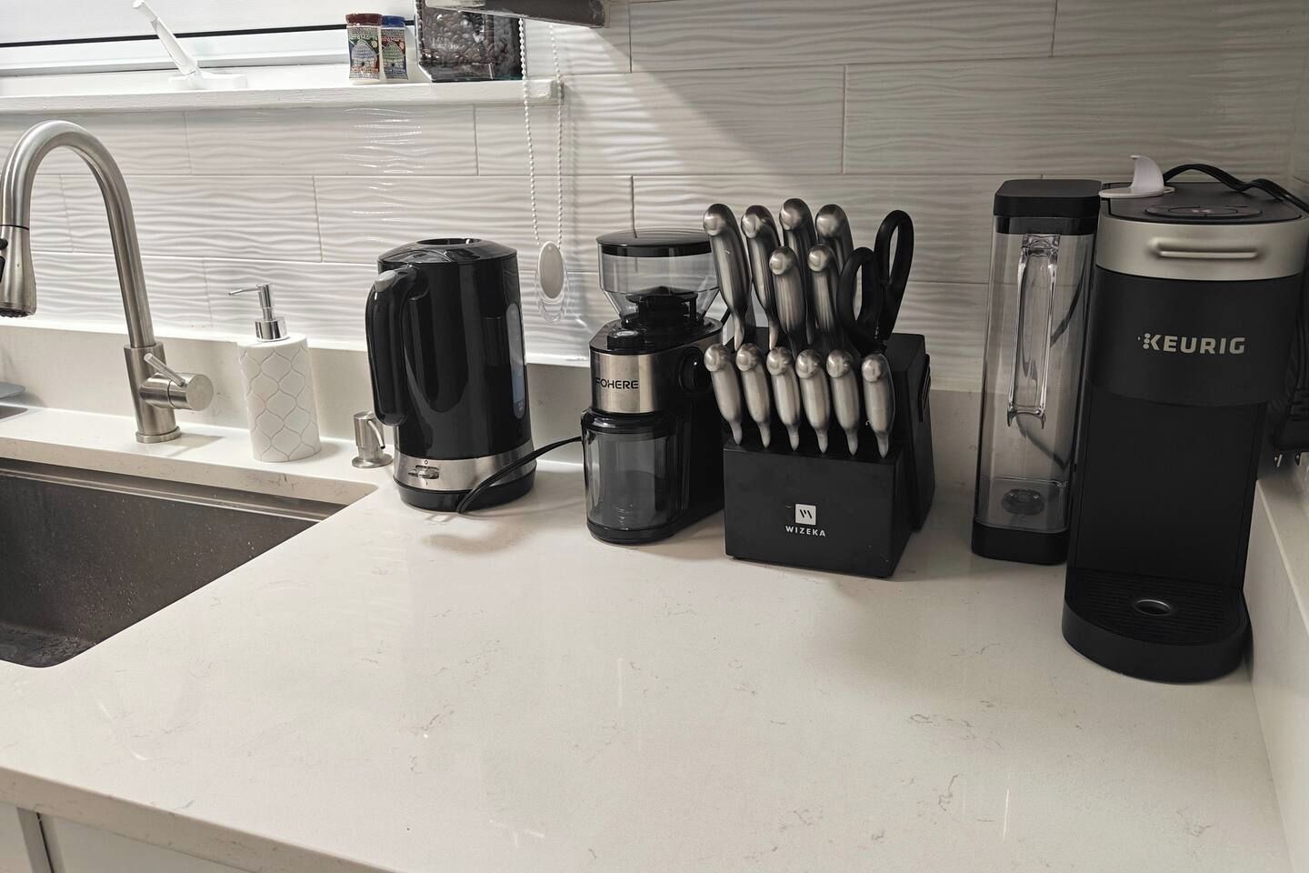 Una encimera de cocina con cafetera, dispensador de agua, bloque de cuchillos y cafetera Keurig.