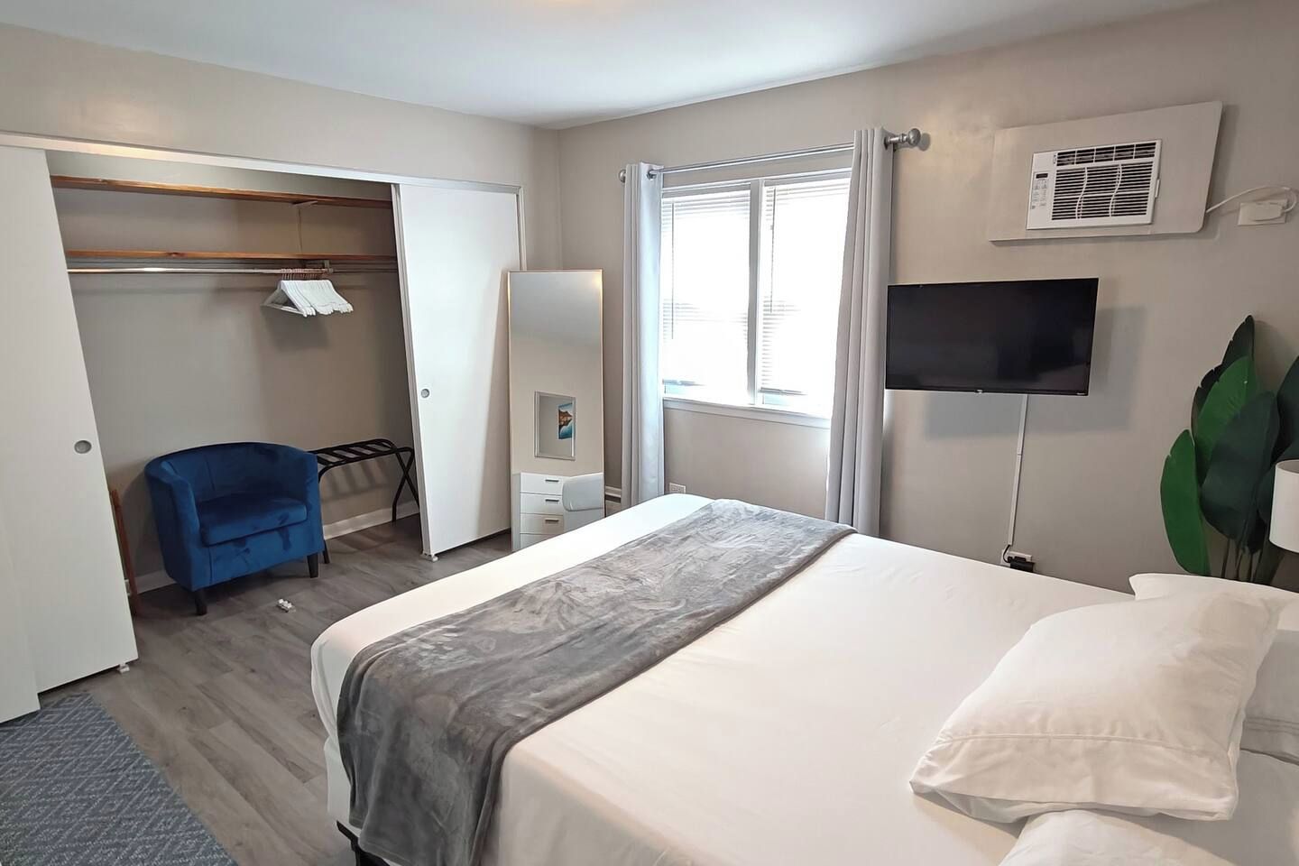 Une chambre d’hôtel avec un lit, une armoire, une chaise, une télévision et une fenêtre avec des rideaux.