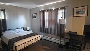 A hotel room with a bed, bedside table, lamp, chair, and a window with curtains.