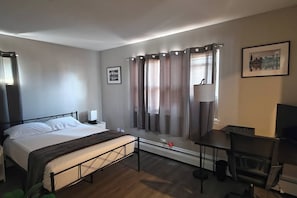 A hotel room with a bed, bedside table, lamp, chair, and a window with curtains.