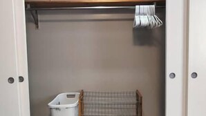A closet with a hanging rack, a laundry basket, and a bench.