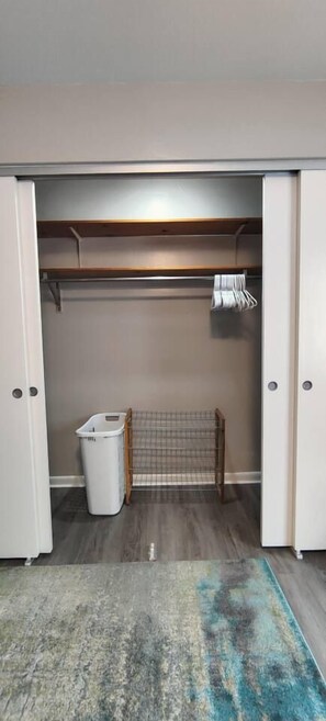 A closet with a hanging rack, a laundry basket, and a bench.