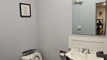 Un baño con inodoro, lavamanos, espejo y un cuadro en la pared.