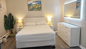 A bedroom with a bed, bedside lamps, a dresser, a large plant, and a painting on the wall. - Greenwood Loft & Rooftop (Waukegan)