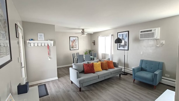 A modern living room with a grey sofa, a blue armchair, and a dining area with a table and chairs. - Greenwood Loft & Rooftop (Waukegan)