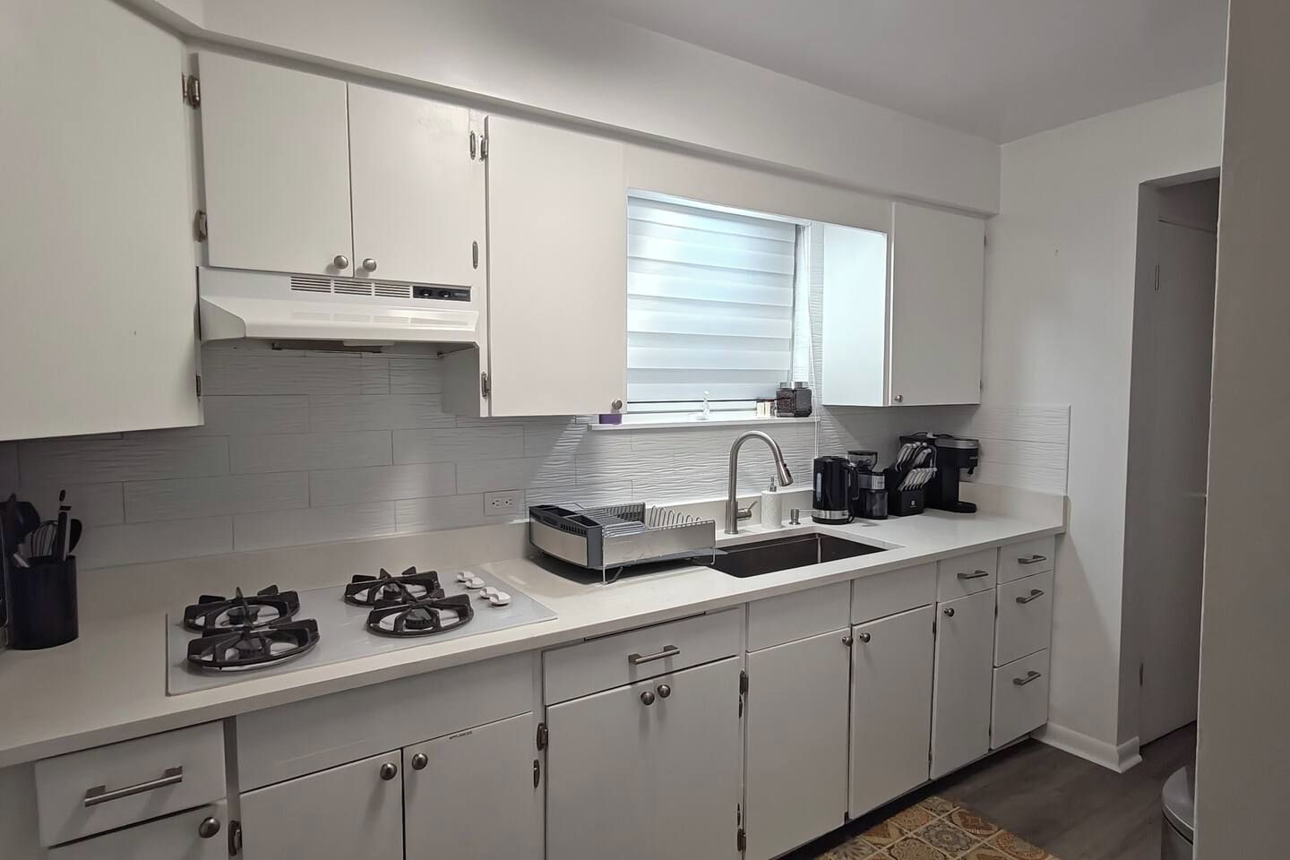 A modern kitchen with white cabinets, a gas stove, a sink, and a window above the countertop.