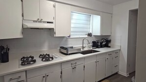 A modern kitchen with white cabinets, a gas stove, a sink, and a window above the countertop.
