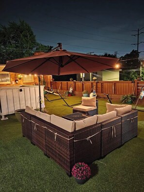 An outdoor patio area with a large umbrella, wicker furniture, and a grill station.
