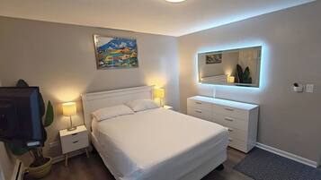 A bedroom with a bed, bedside tables, a dresser, a mirror, and a painting on the wall.