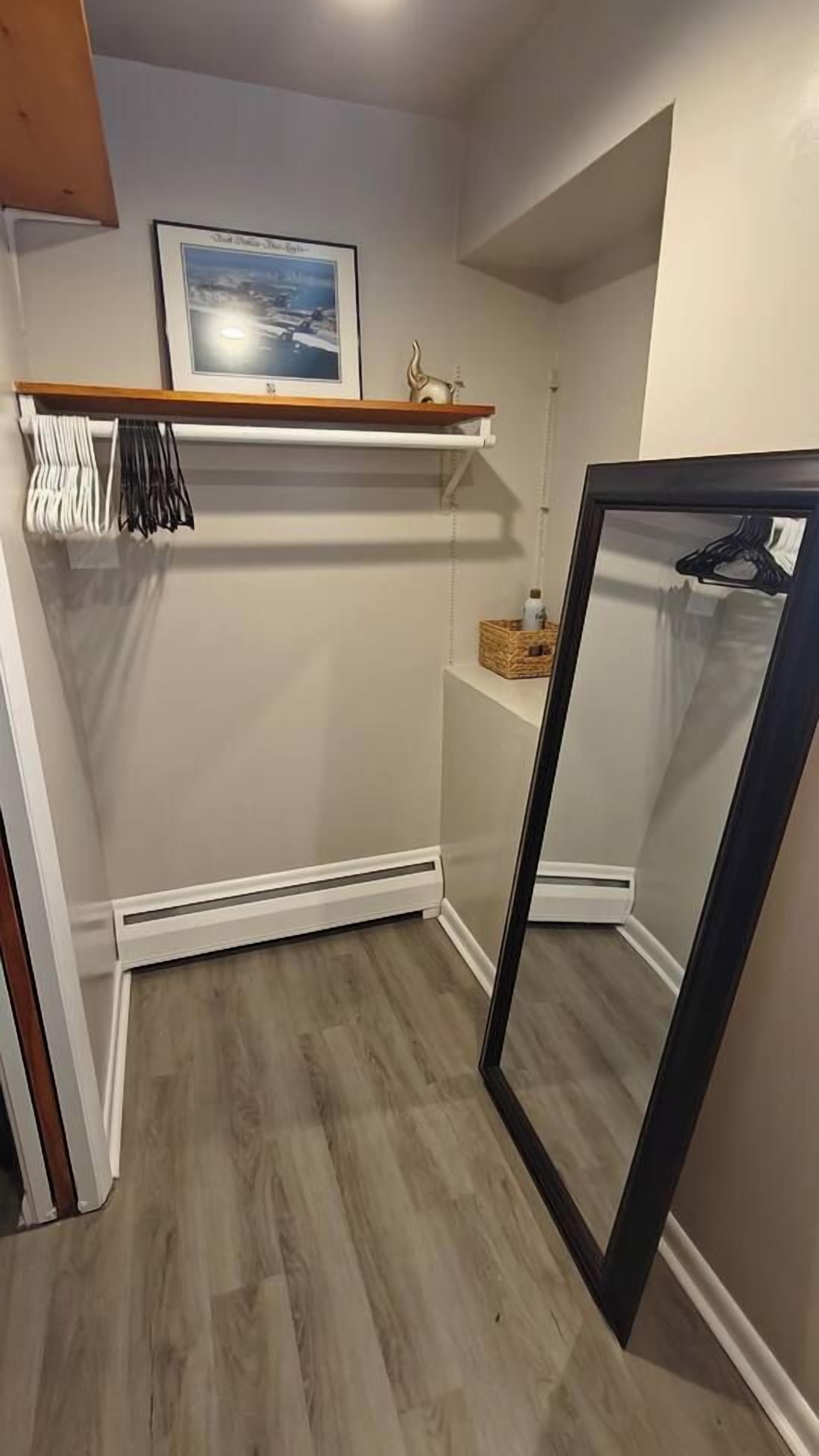 Un petit placard fermé, avec une étagère en bois, une tringle pour suspendre les vêtements et un miroir.