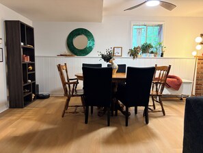 A dining area with a wooden table and chairs, a dark bookshelf, a green decorative item on the wall, and a window with plants. - 4-bedroom Village of Dryden house/ 9 mi. to Greek Peak skiing, Cornell, Cortland (Dryden)