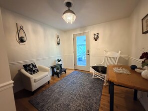 A living room with a white sofa, a small side table with a plant, a wooden dining table with a chess set, and a door leading outside. - 4-bedroom Village of Dryden house/ 9 mi. to Greek Peak skiing, Cornell, Cortland (Dryden)