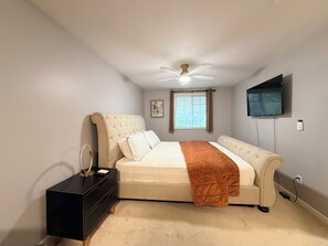 Ein Schlafzimmer mit einem Bett, einem Nachttisch, einem Deckenventilator, einem Fenster und einem Fernseher.