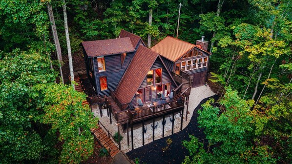 A cabin with a deck, surrounded by dense forest. - RRG cottage - cave fire pit, hot tub, & pool table (Stanton)